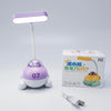 A small desk lamp shaped like a purple and white submarine sits beside its retail box and a USB charging cable on a clean light gray studio background. The lamp has a rectangular illuminated head, a white stand, a clear dome, the number 07 on the front, and a cartoon face inside the dome.